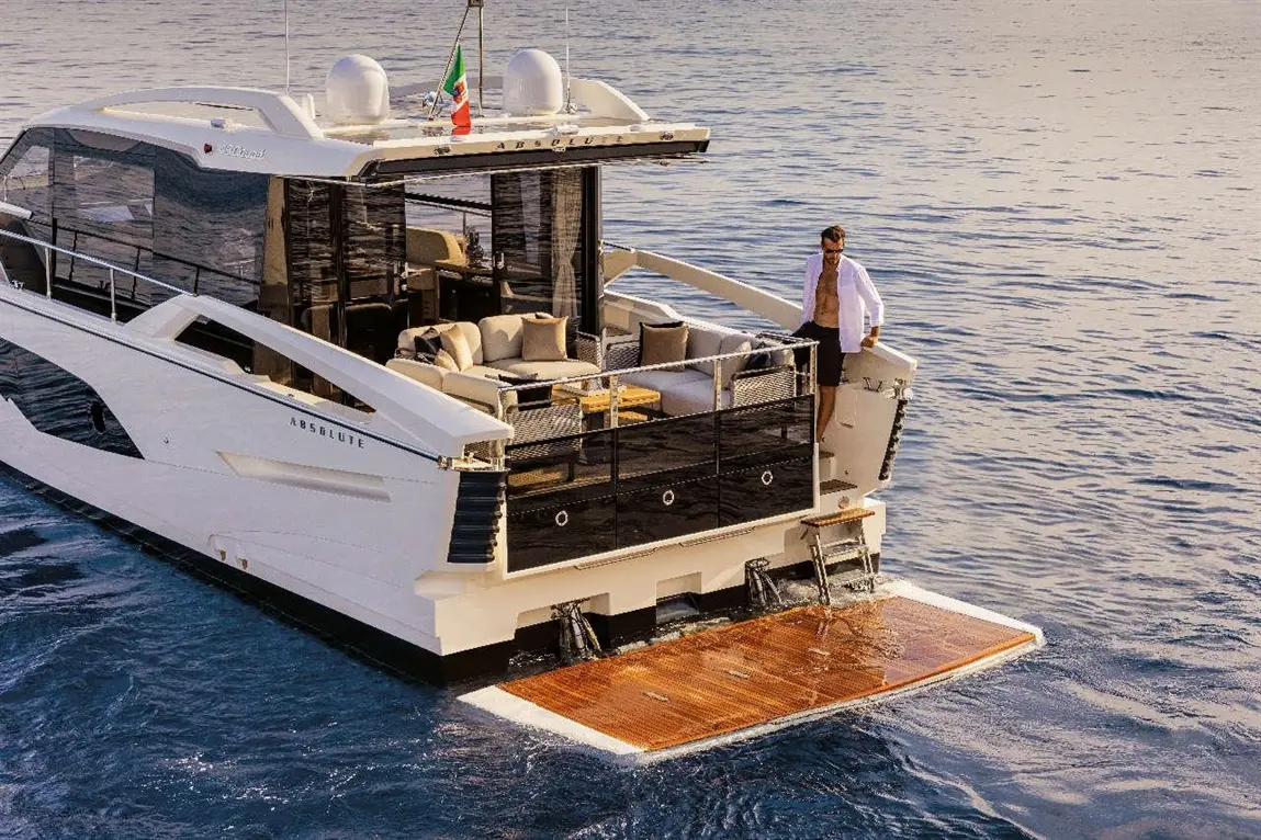 Luxury motor yacht named 'Absolute' with a man in a white shirt on the deck above a wooden swim platform.